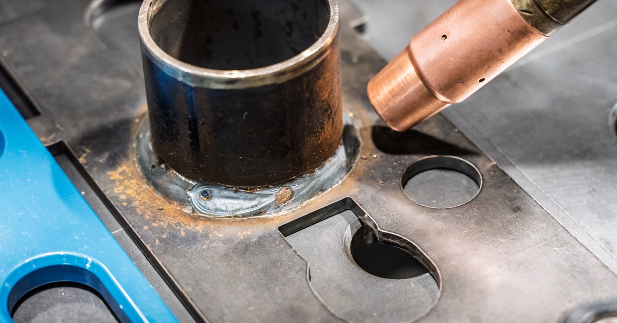 A copper welding tip positioned near a black metal tube with a visible freshly welded seam along its base.