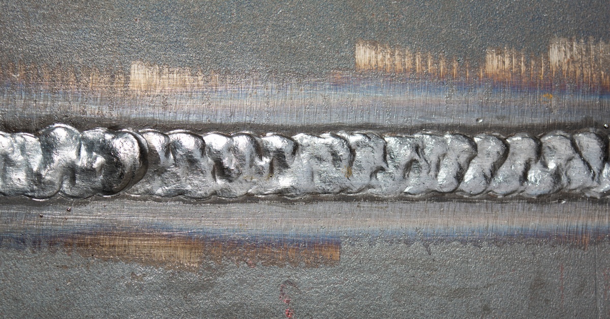 Two fused plates display a rippled weld joint with visible discoloration and surface finishing marks above and below.