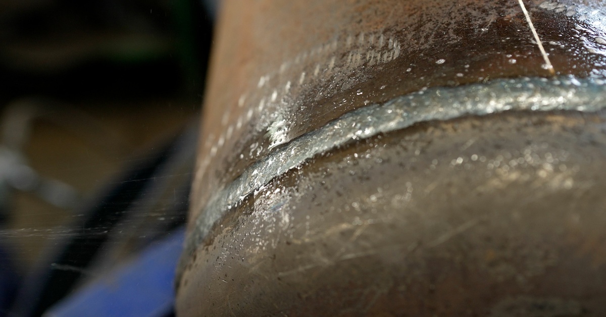A copper-colored pipe shows a wet, silver weld seam running across its surface with visible moisture reflecting light.
